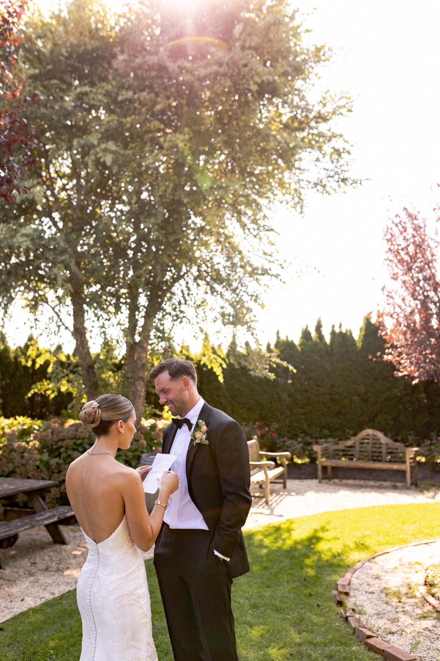 A romantic couple in formal wedding attire share an intimate moment in a sunlit garden during golden hour.