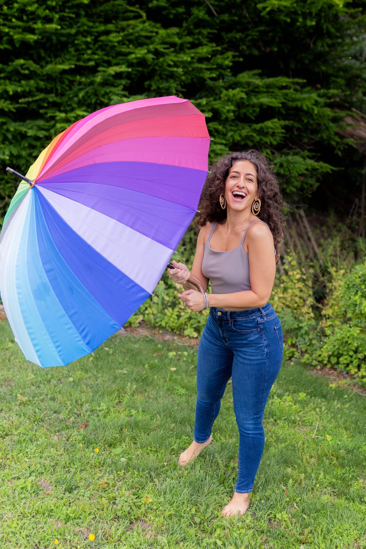 Playful sequence with a colorful rainbow umbrella being twirled on a grassy lawn in summer.