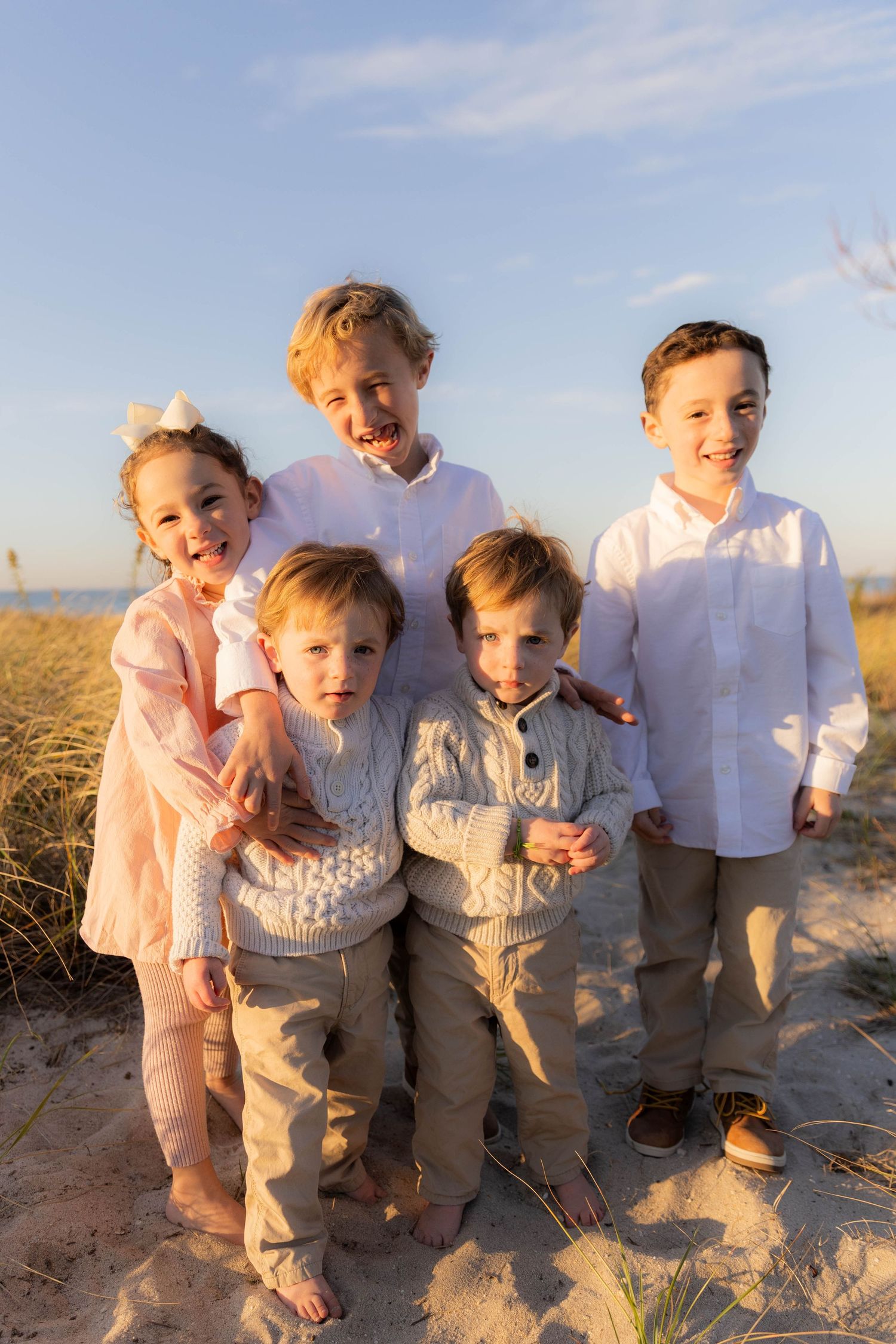 Children in coordinated outfits laughing together on sandy beach during sunset photoshoot.