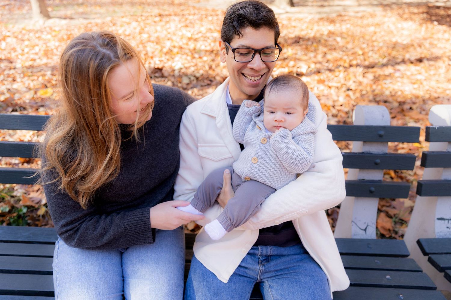 Family sitting together on wooden bench surrounded by autumn foliage.