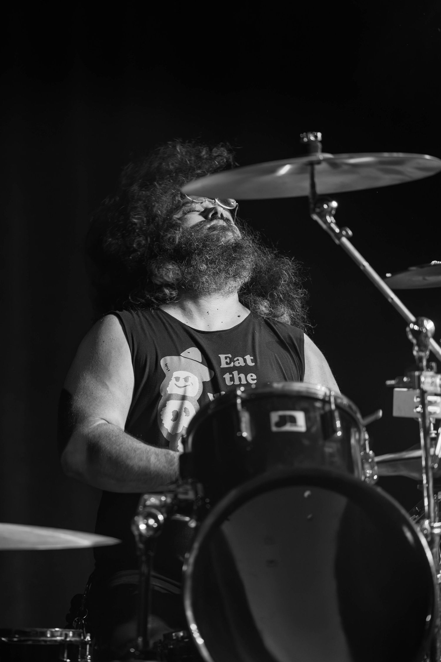Drummer performing on stage in dramatic black and white lighting.