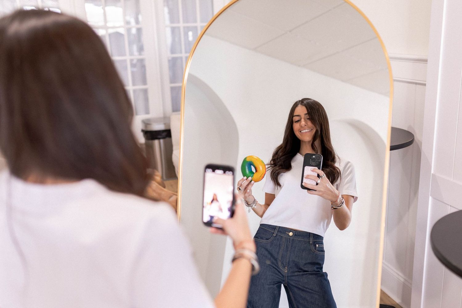 Person in white t-shirt and jeans taking creative photos with pizza and produce against white wall.