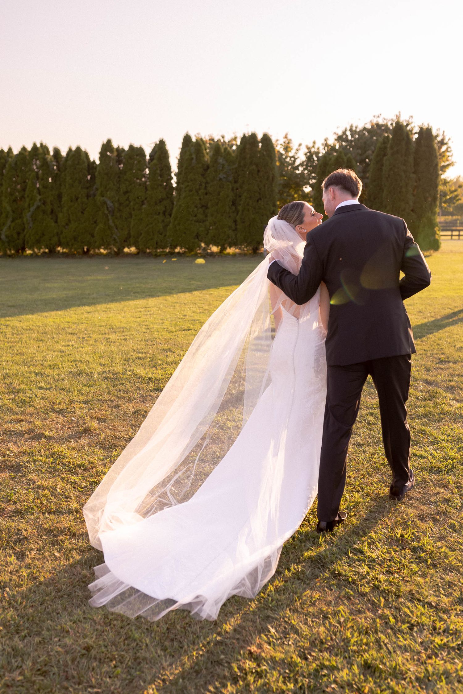 A wedding couple and photographer create a series of romantic sunset portraits in a grassy field.
