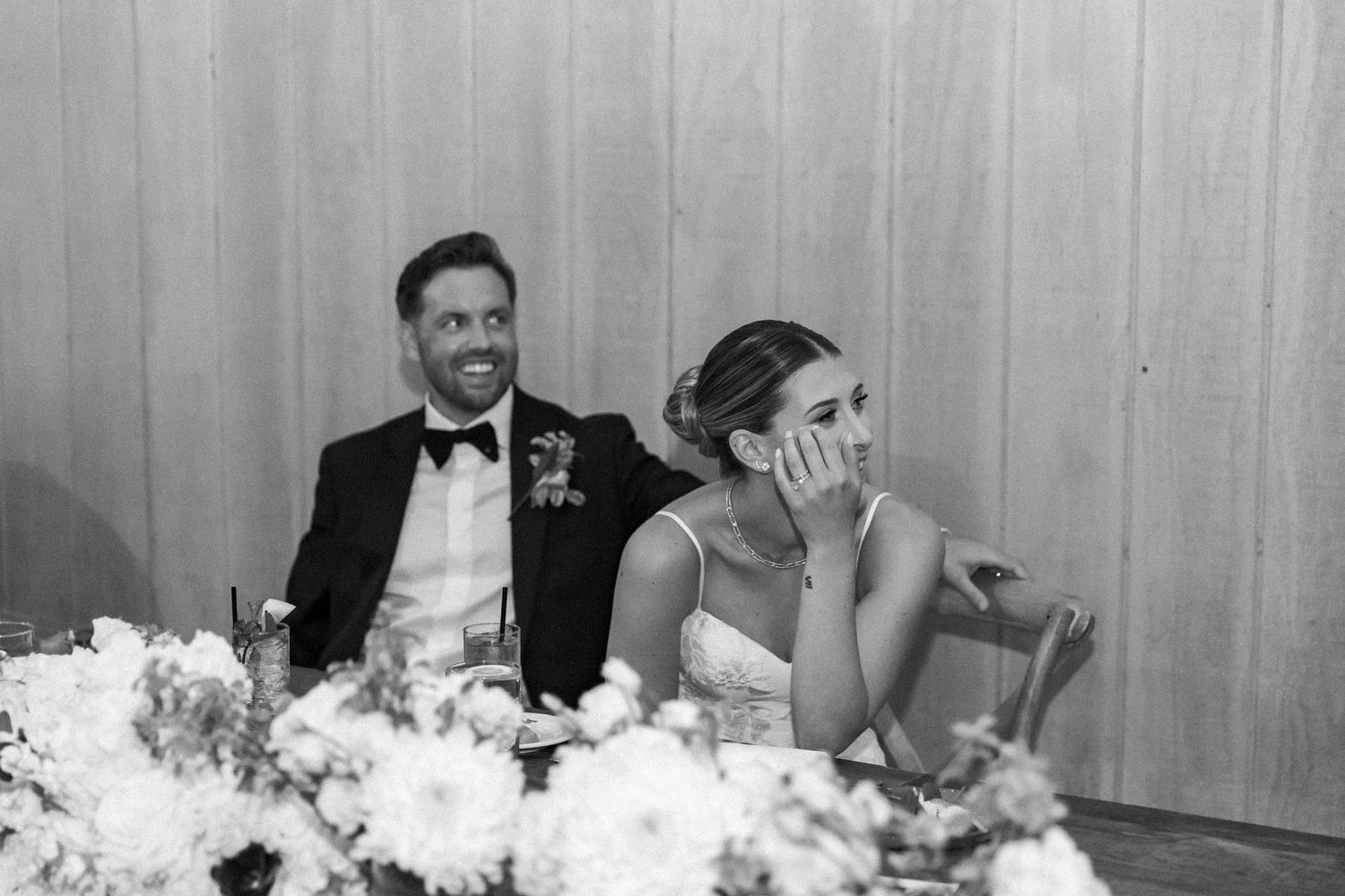 A black and white wedding reception photo shows guests seated at decorated tables with floral centerpieces.