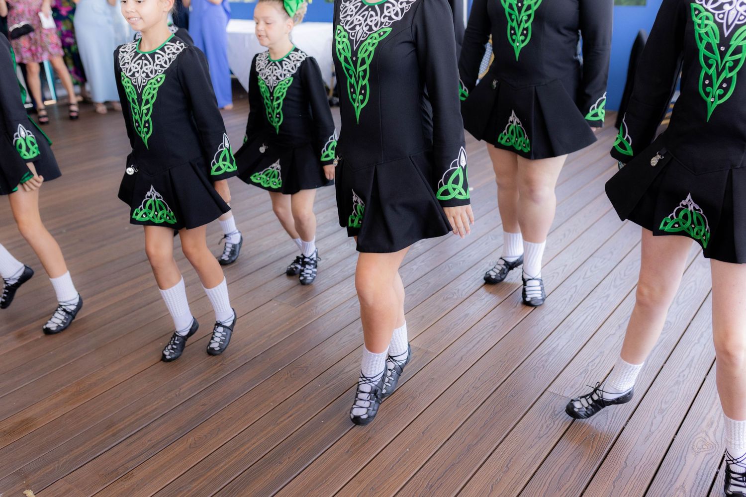 Irish dancers in black and green costumes perform traditional steps on a wooden floor during a performance.
