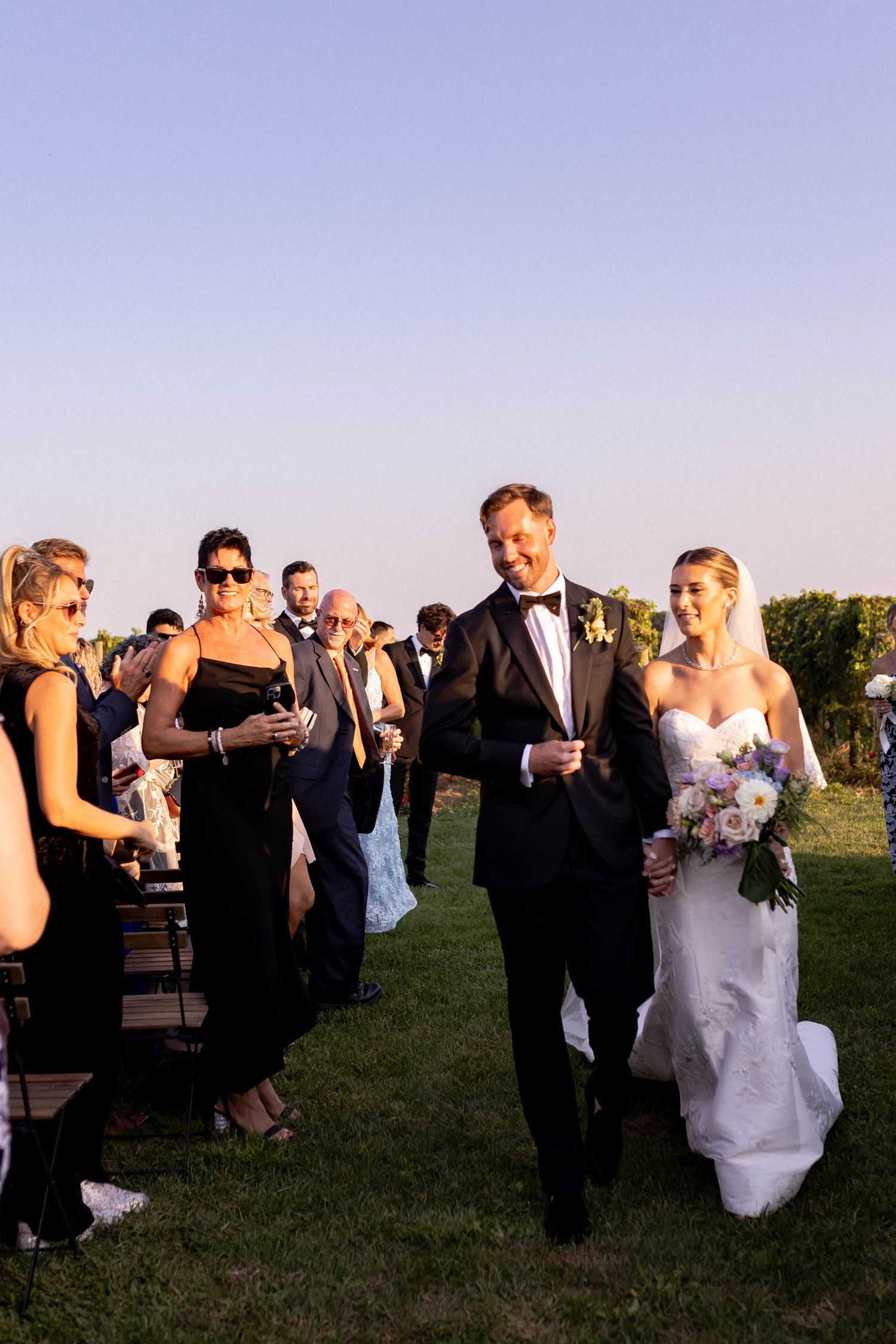 Wedding guests celebrating on a grassy field during a late afternoon reception.
