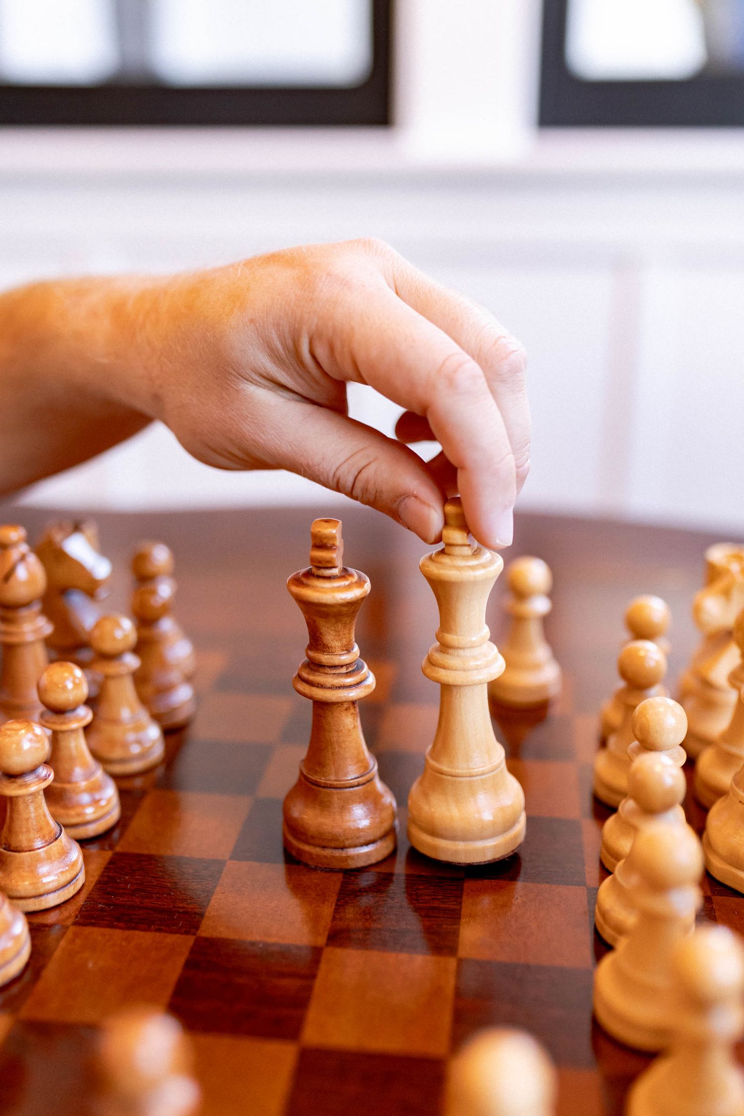 Hand moving wooden chess pieces on a traditional wooden chess board during gameplay.