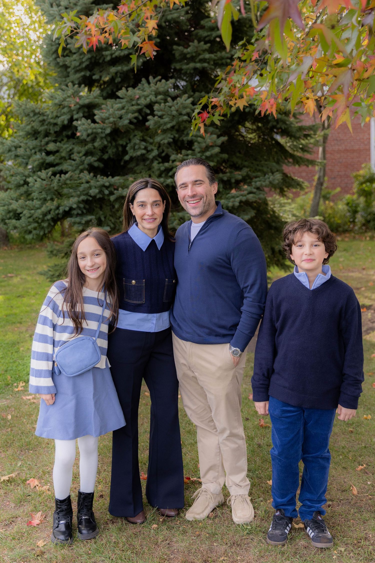 Family group wearing navy and blue casual attire poses under fall foliage.
