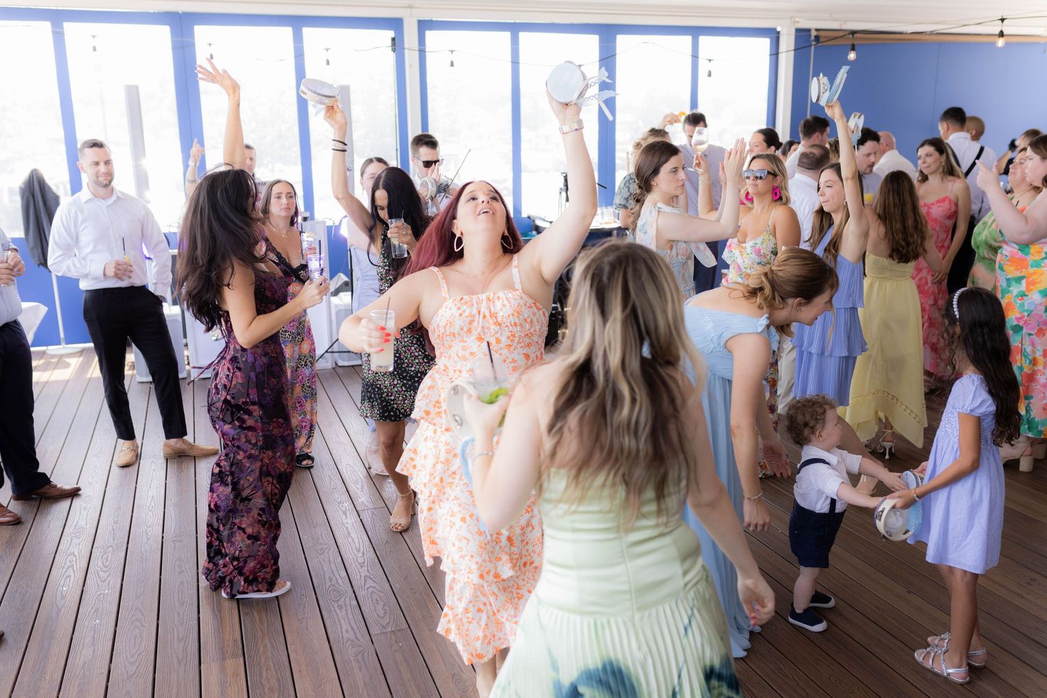 Wedding guests gather on a wooden deck overlooking the ocean during an outdoor reception celebration.