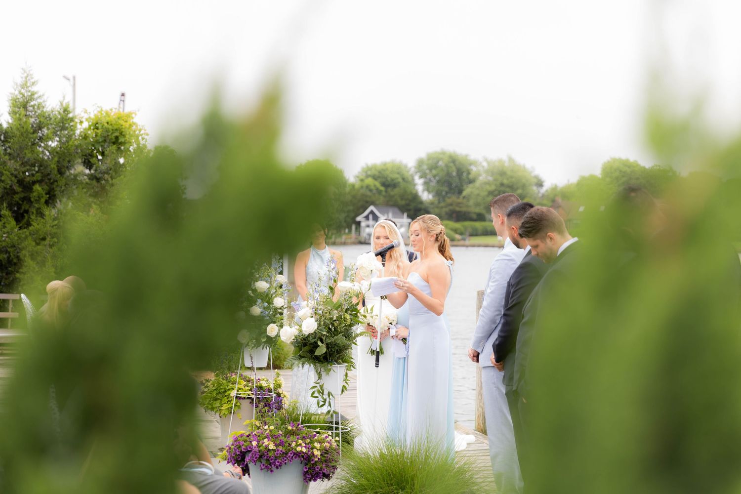 Outdoor wedding ceremony framed by green foliage with guests in formal attire gathered for the celebration.