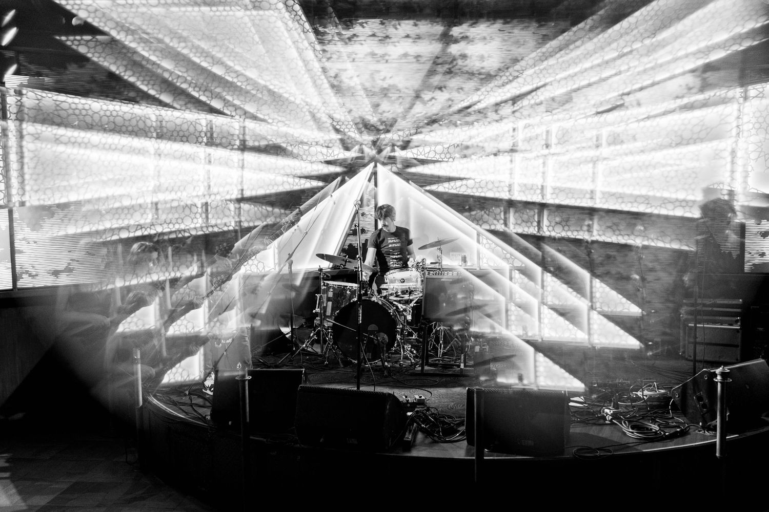 Stark white lighting beams form geometric patterns against a black background in a concert setting.