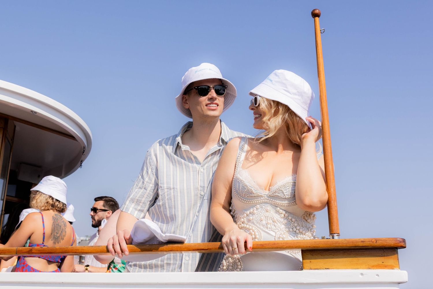 Two people in sunhats and summer attire enjoying a sunny day aboard a boat deck.