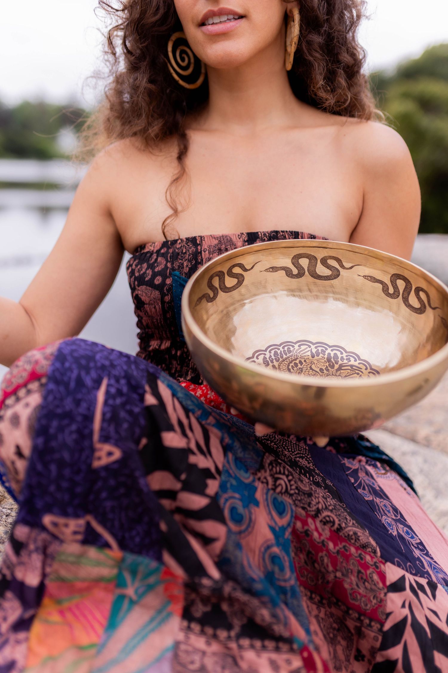Close-up of decorative singing bowl held with patterned dress and jewelry visible.