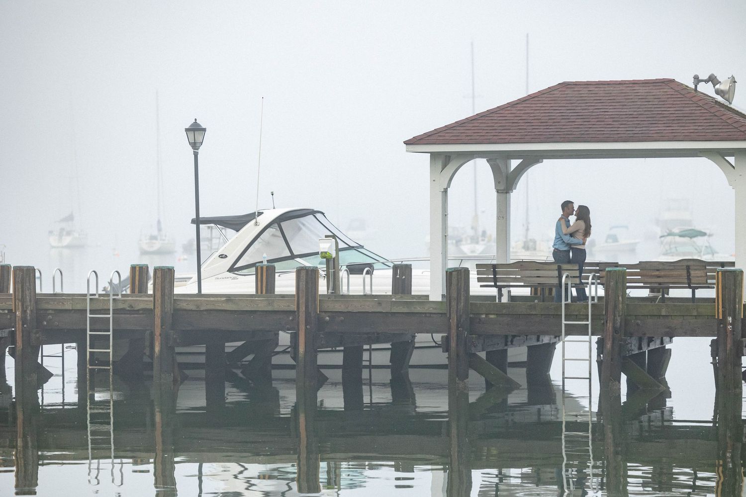 A long wooden pier extends over calm water with a gazebo at the end and boats docked along the side.