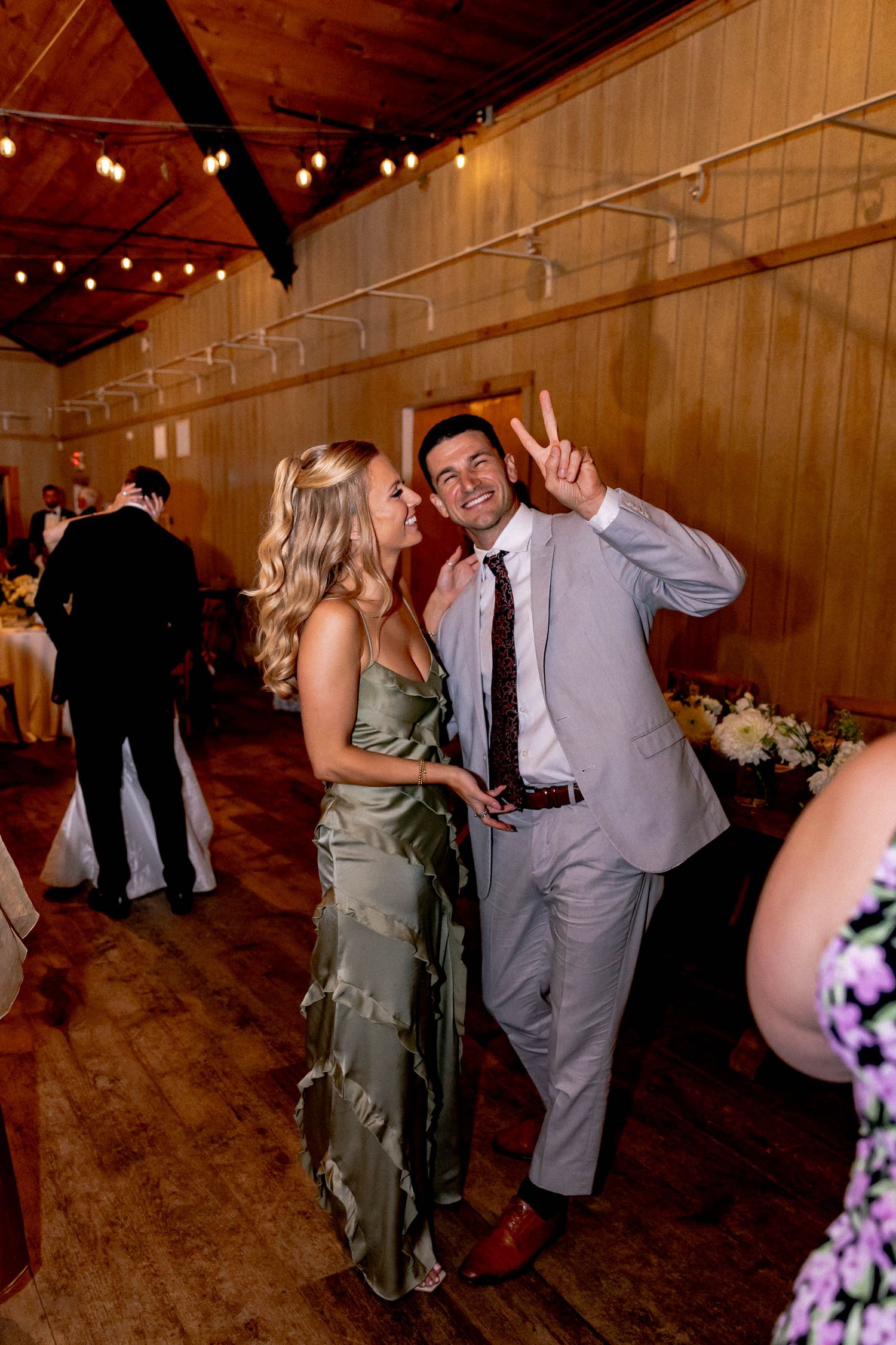 Couples dancing together during a wedding reception in a warmly lit wooden barn venue.
