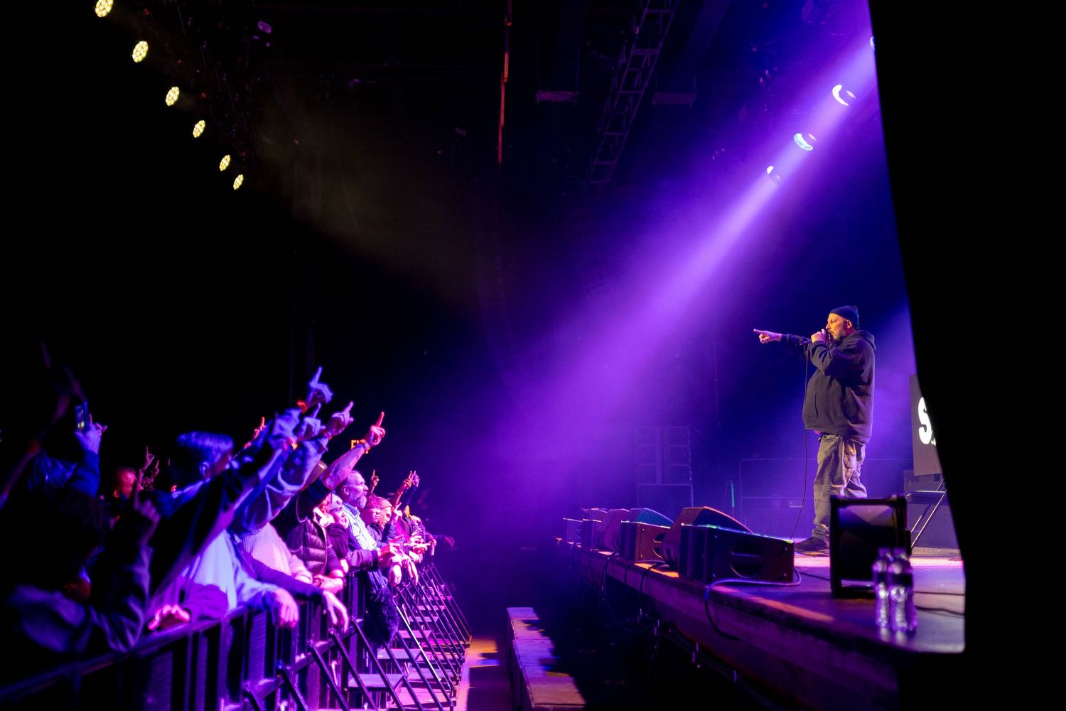 Wide shot of concert stage with dramatic purple spotlights creating atmospheric ambiance.