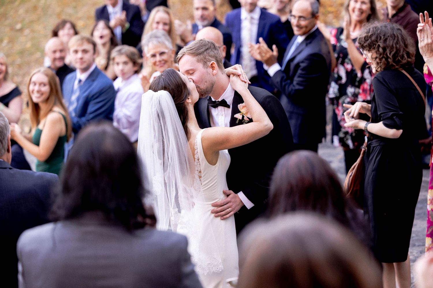 A romantic moment shared between newlyweds during their outdoor wedding ceremony as guests look on.