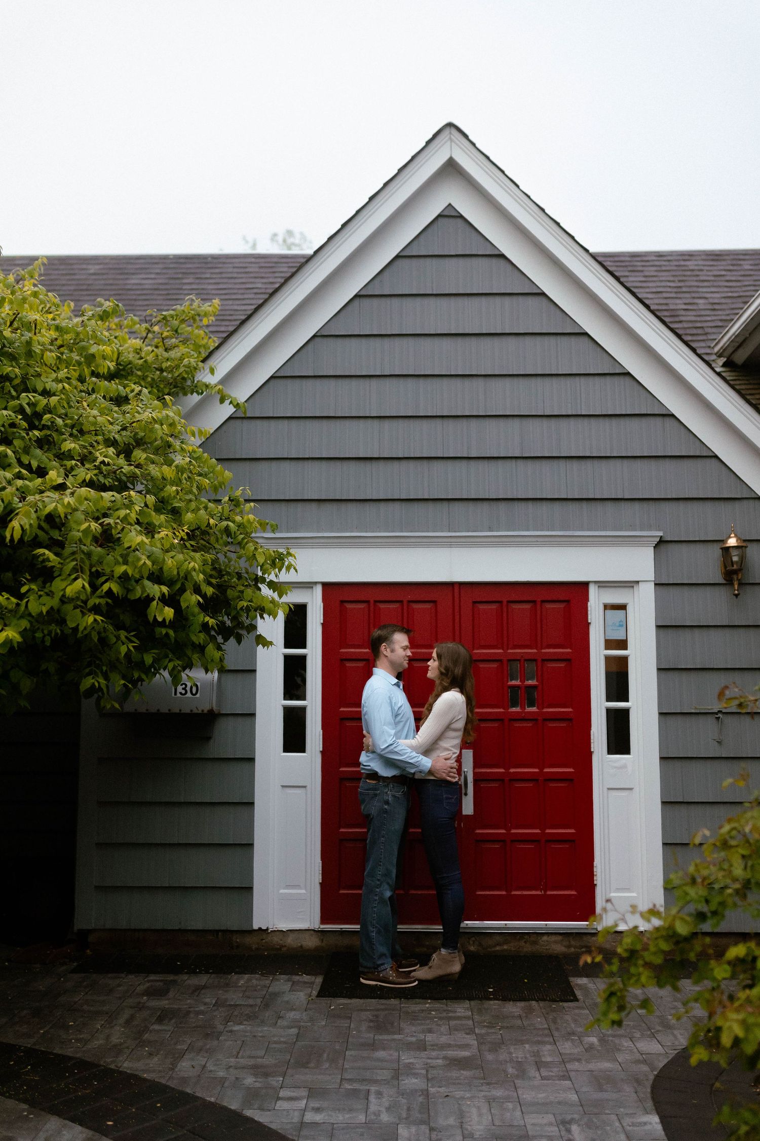 A series of engagement photos taken in front of a gray house with a striking red door and stone walkway.