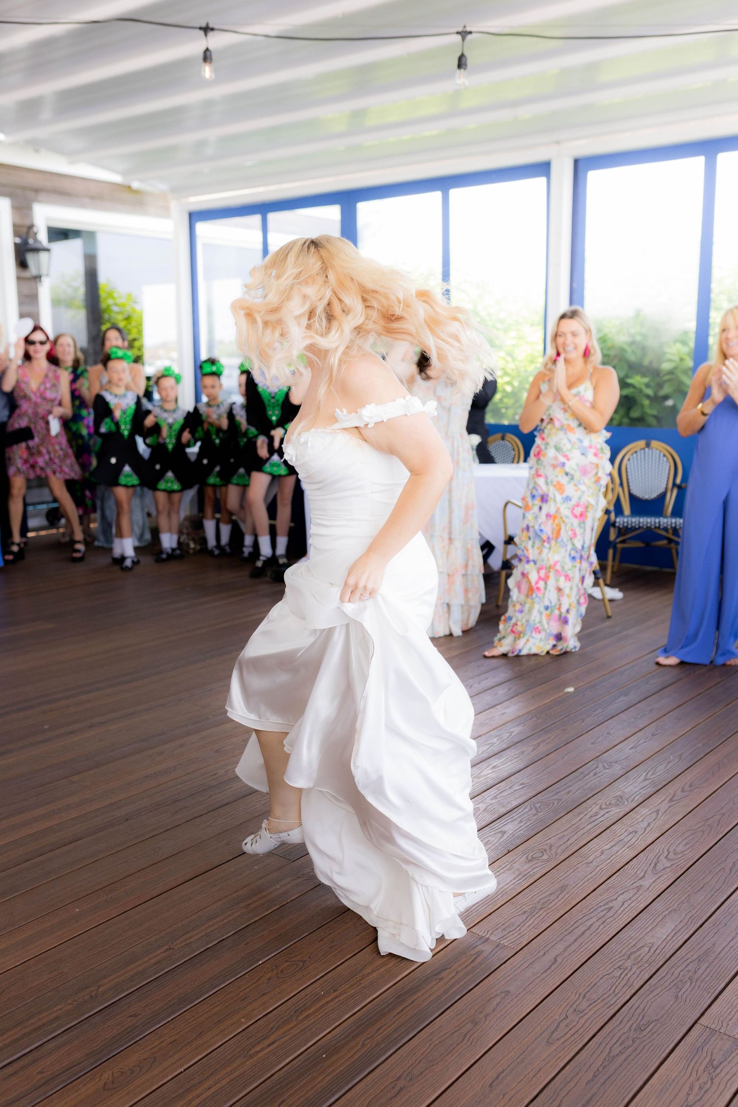 A joyful dance scene at a wedding reception with attendees in blue and floral dresses on a wooden floor.