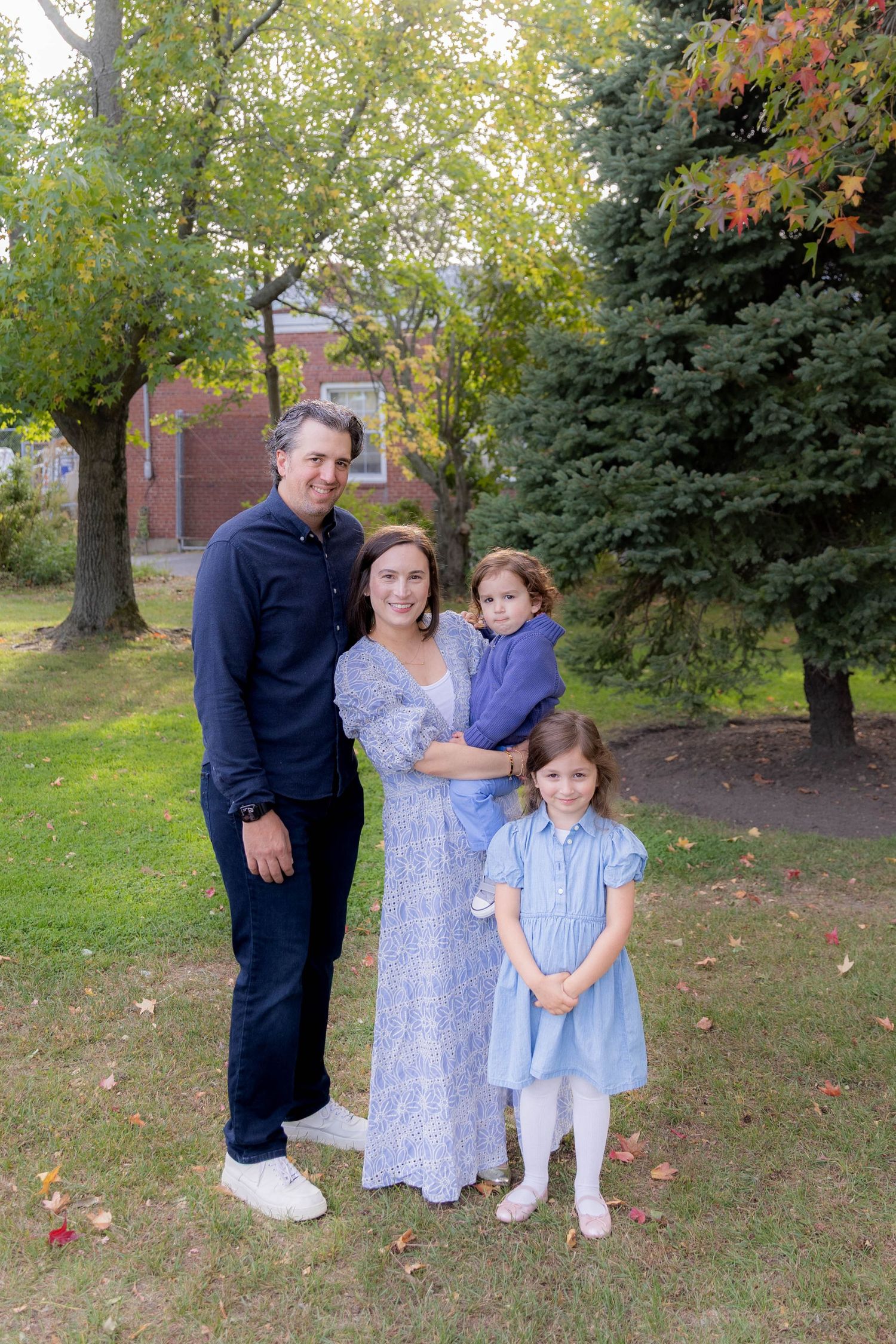 Family members in coordinating blue outfits pose together on autumn lawn.