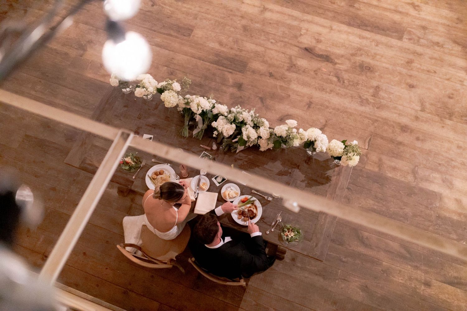 A rustic wedding venue with wooden beams, chandeliers, and white floral decorations creates an elegant atmosphere.