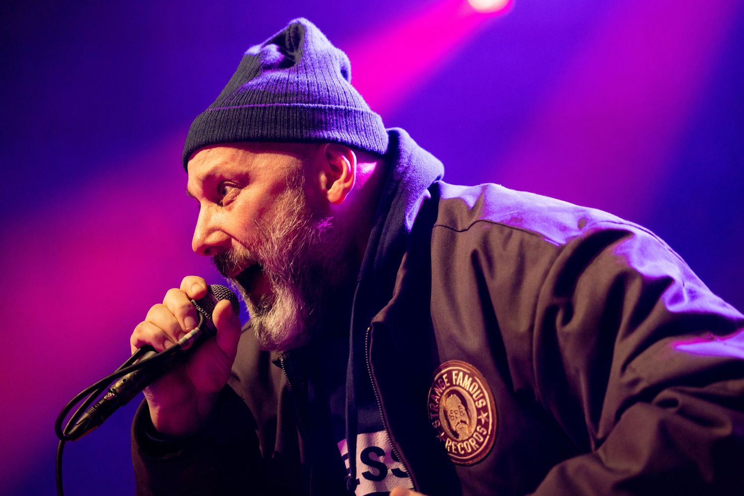 Close-up profile shot of performer in beanie hat under dramatic purple stage lighting.