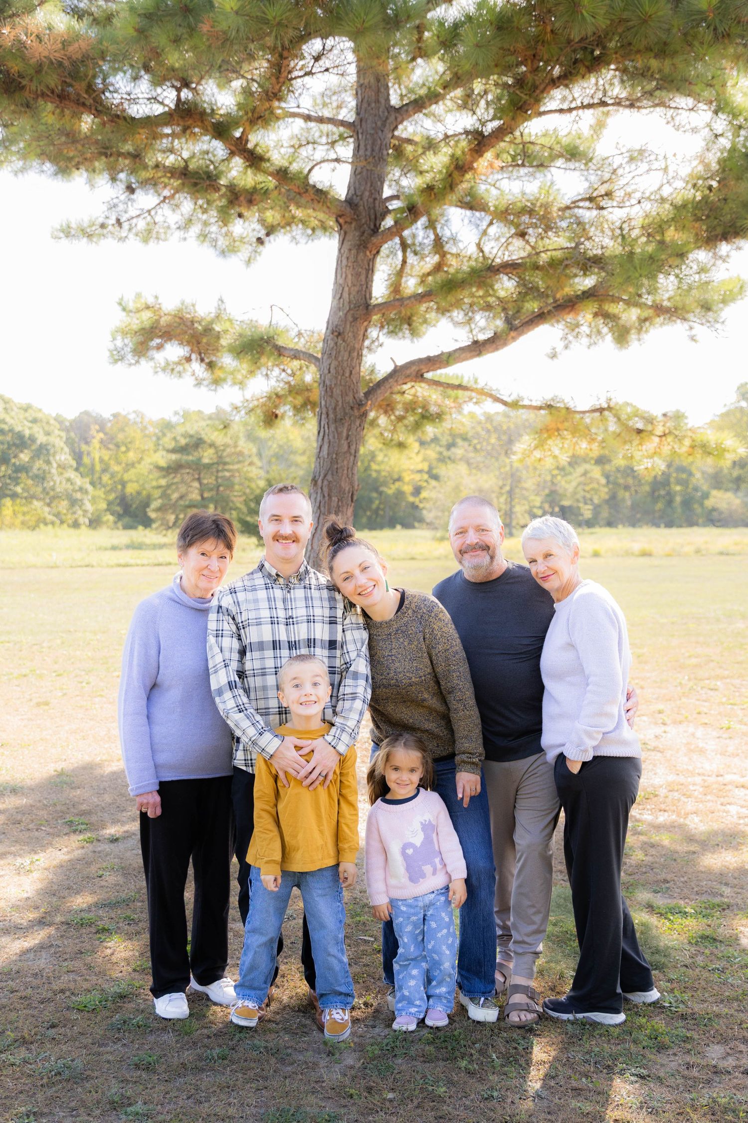 Family members pose together under tall pine trees in a grassy field.