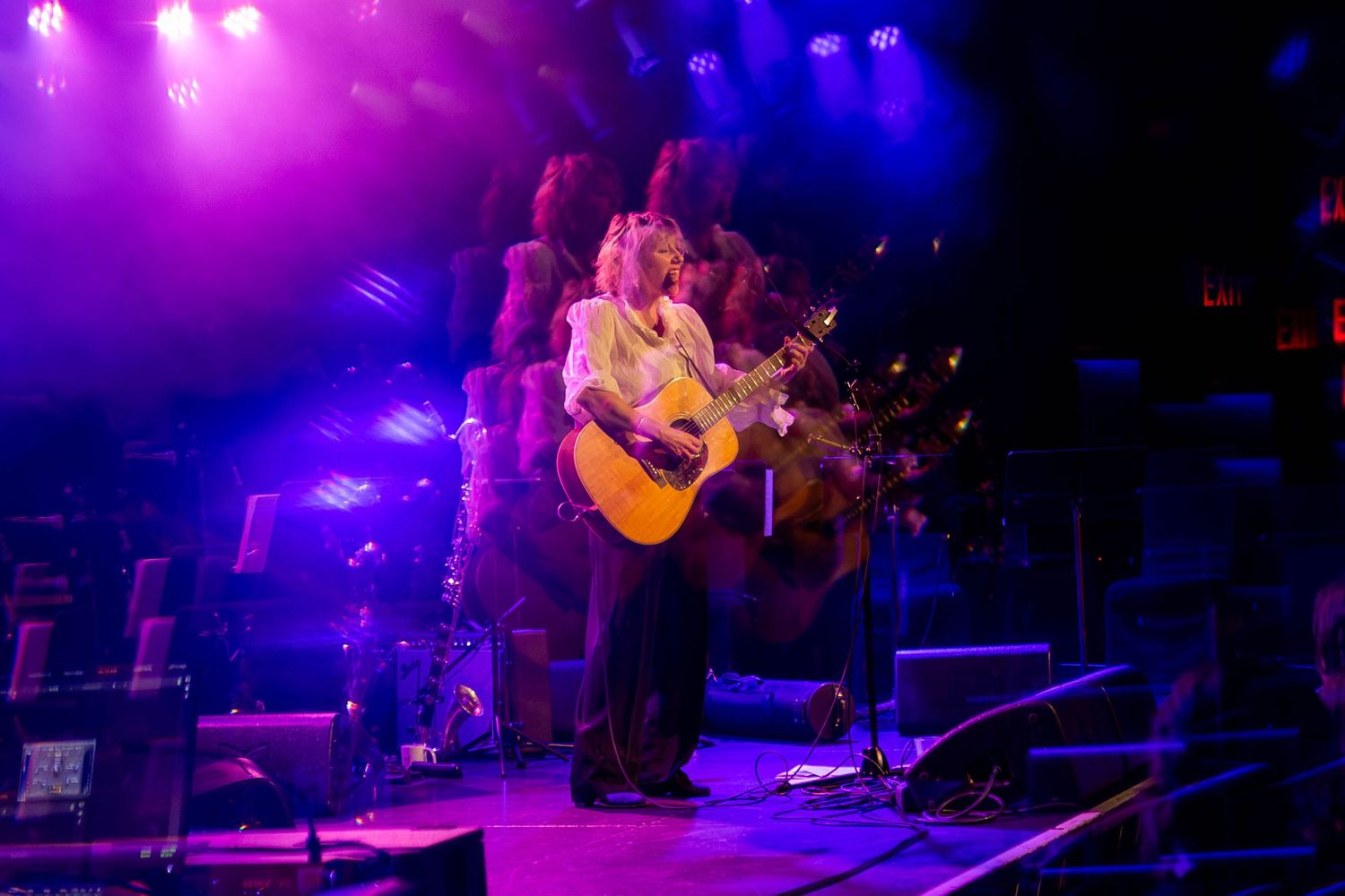 Stage performance captured in vibrant purple and blue lighting with atmospheric smoke effects.