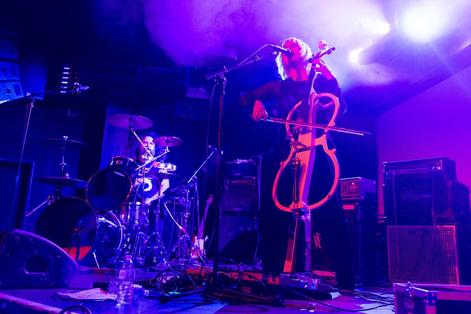 Concert stage setup with instruments and equipment bathed in purple lighting effects.
