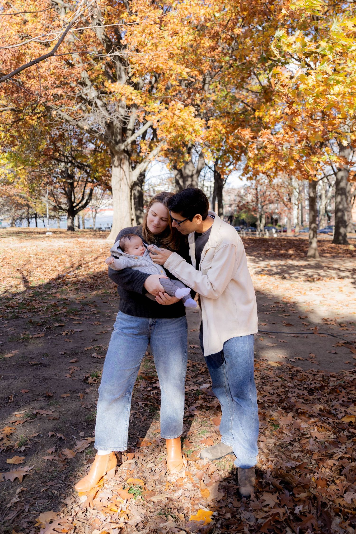 Family sharing tender moments on fallen leaves during autumn photoshoot.