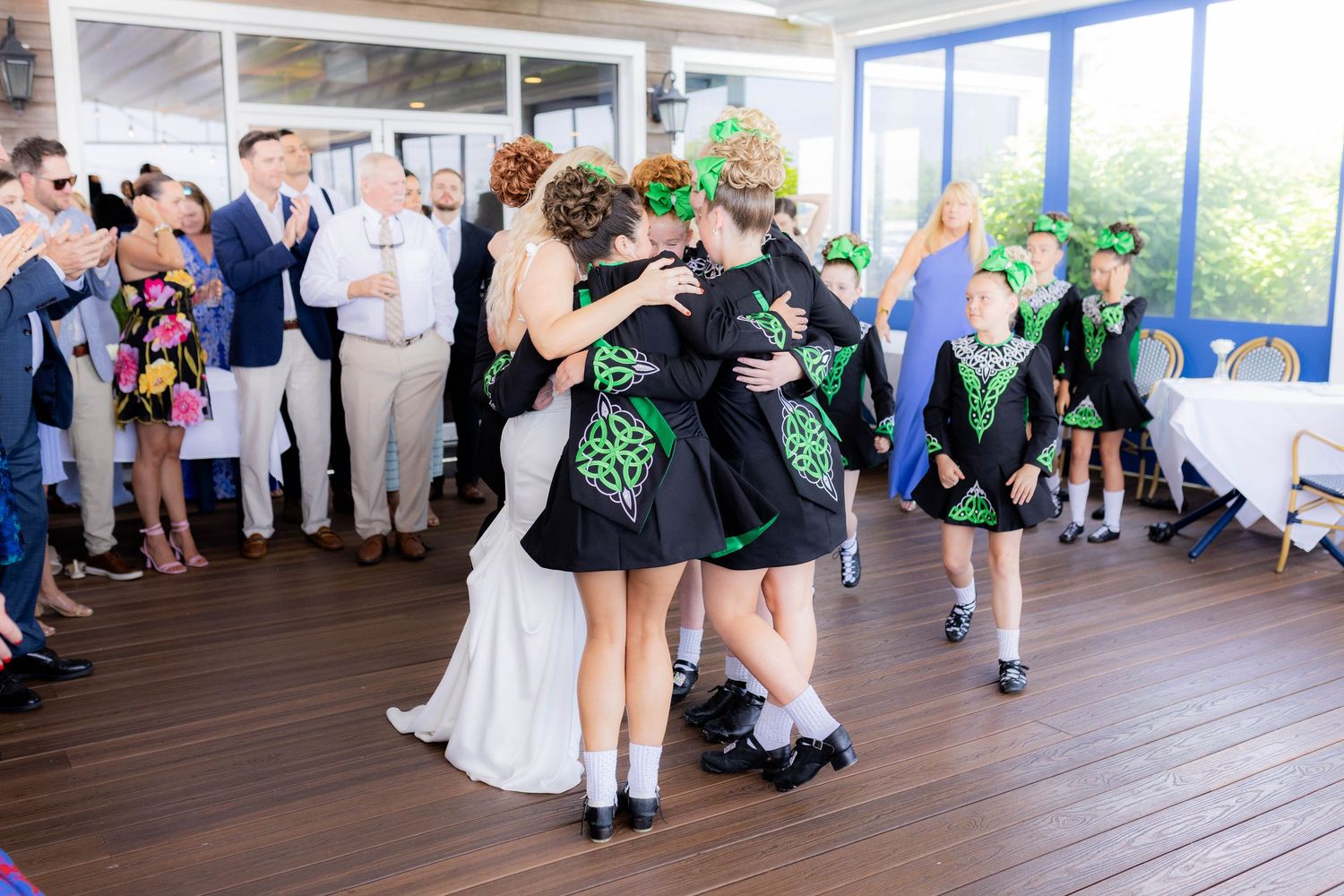 Irish dancers perform traditional dance at a wedding reception on a wooden deck surrounded by guests.