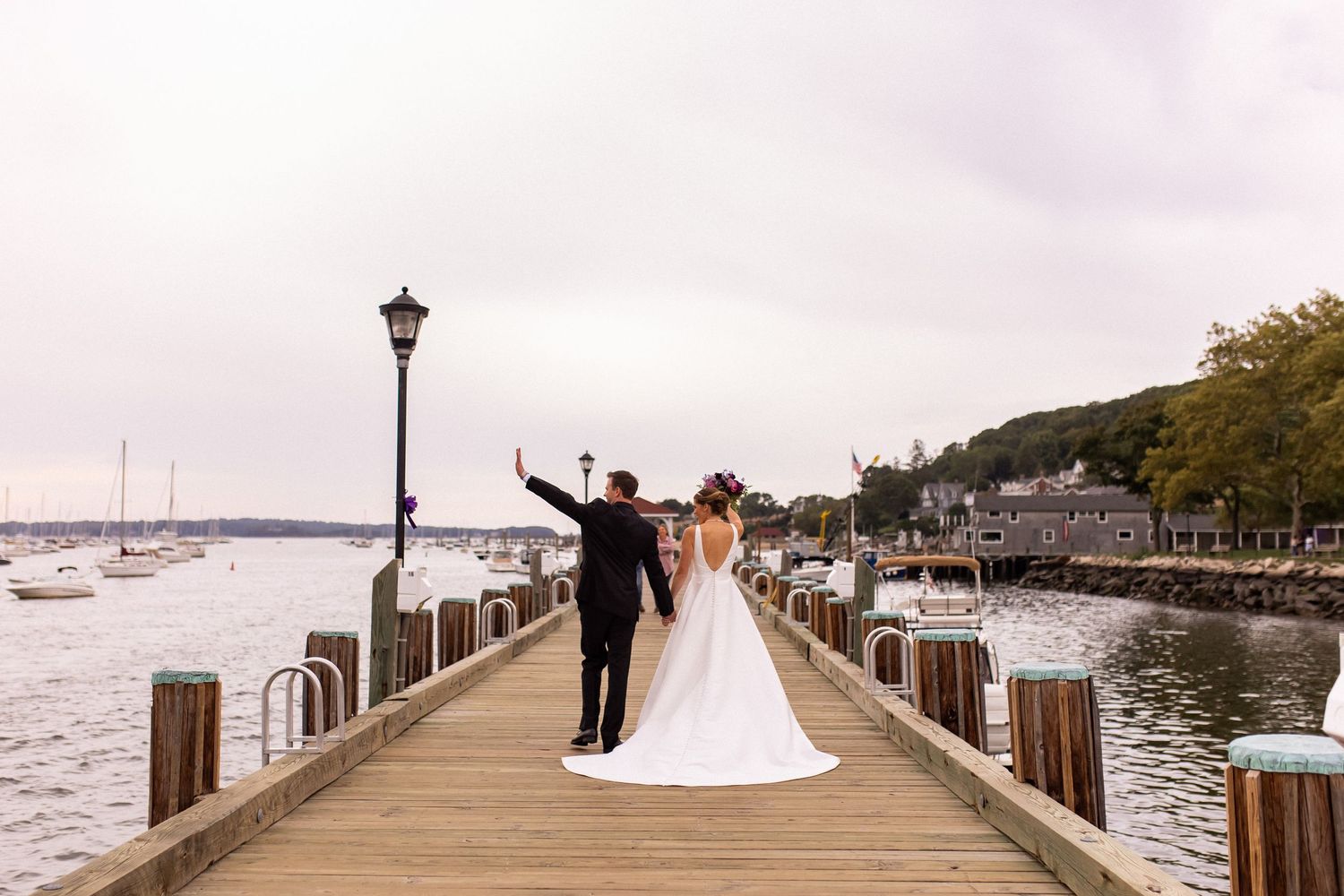 A scenic waterfront boardwalk with wooden posts and lamp posts stretches along the harbor on a cloudy day.