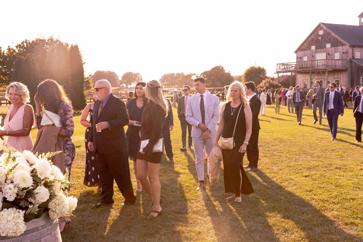 Wedding guests walking across a grassy field at sunset with a white tent in the background.