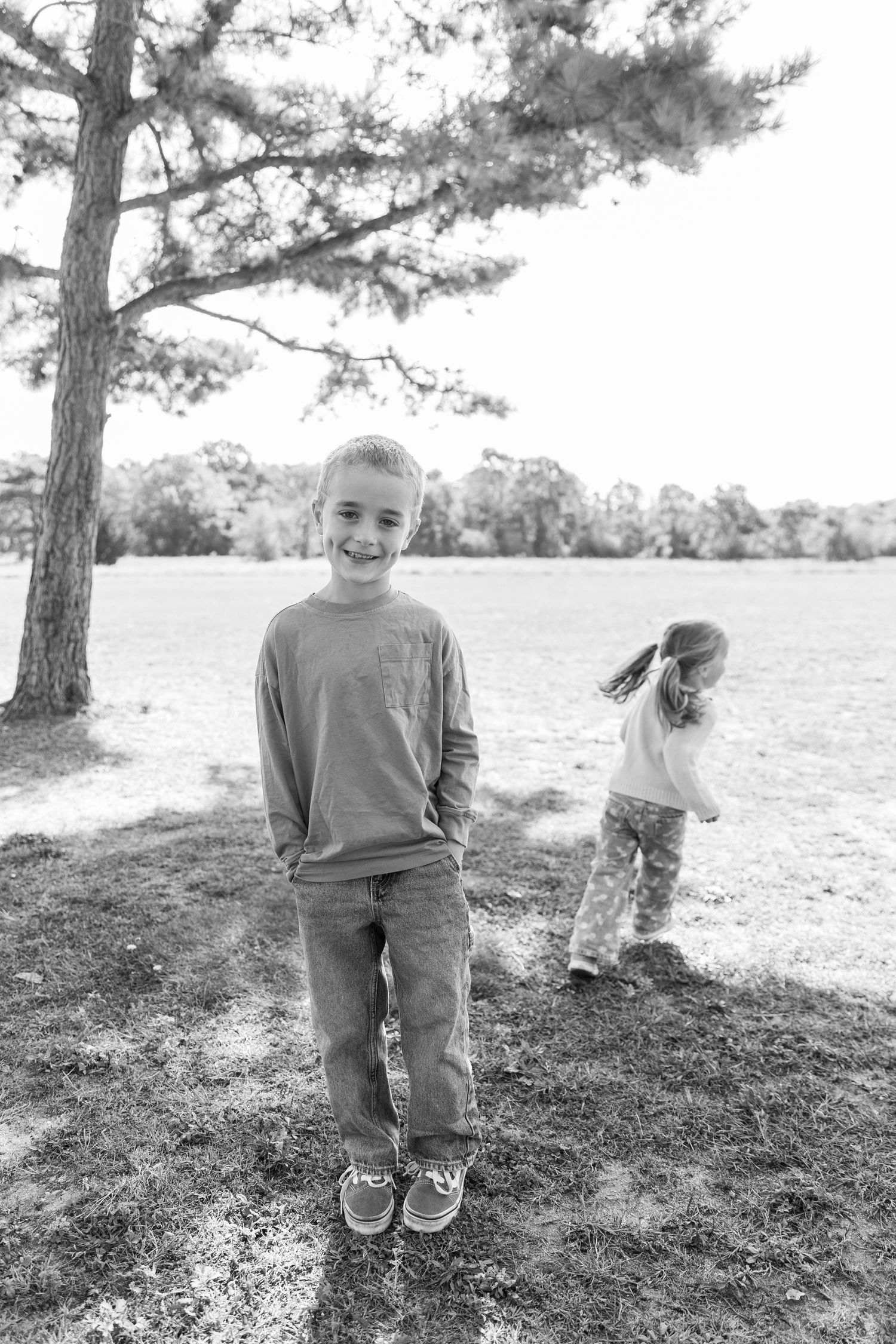 Black and white portraits of children playing on grassy hill under pine trees.