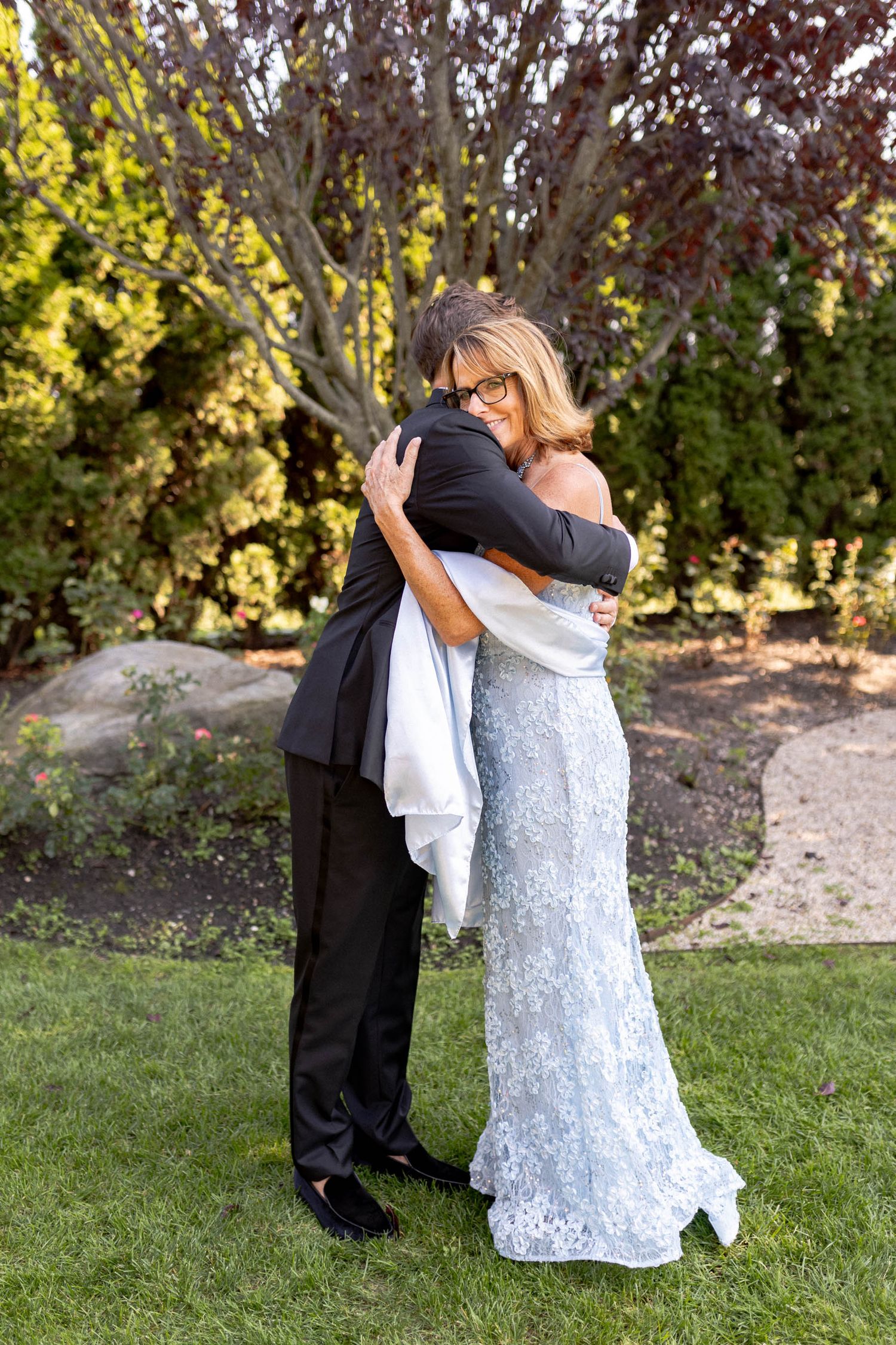 A couple in formal attire embrace in a romantic sequence of photos on a grassy lawn with trees in the background.