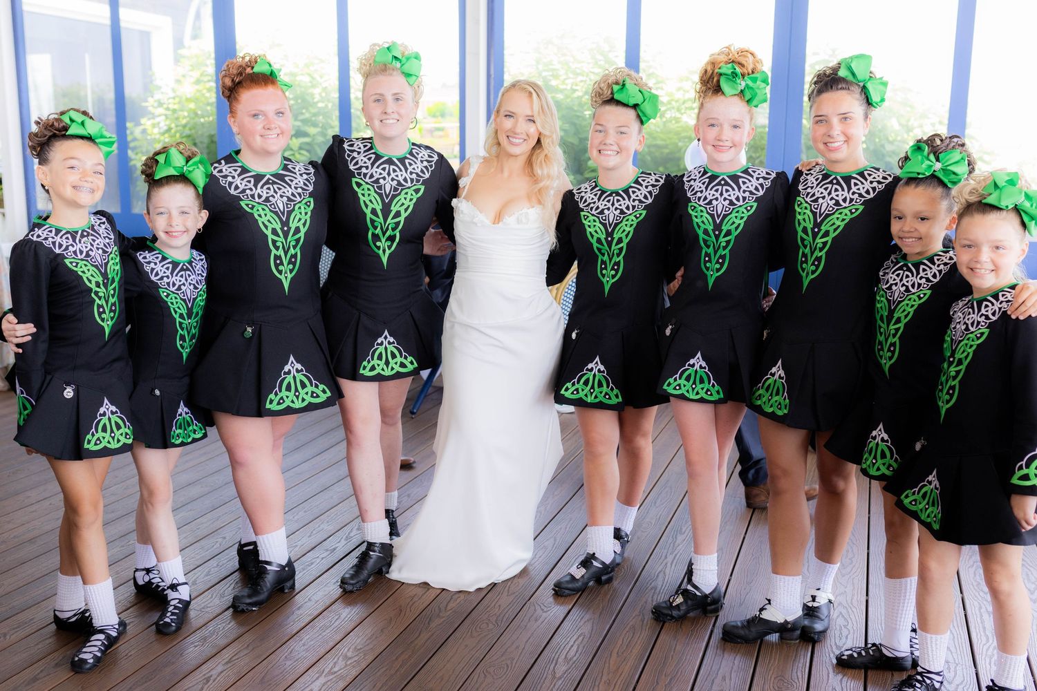 Wedding party with Irish dancers in matching black and green outfits posing together on a deck.