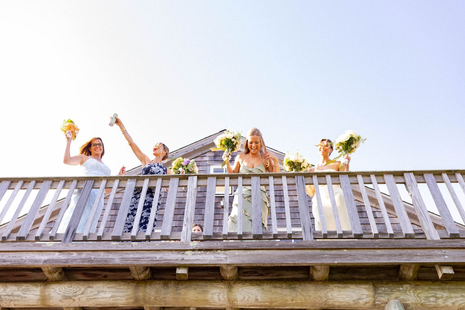 A group of people celebrating on a balcony with raised arms against a bright sky background.