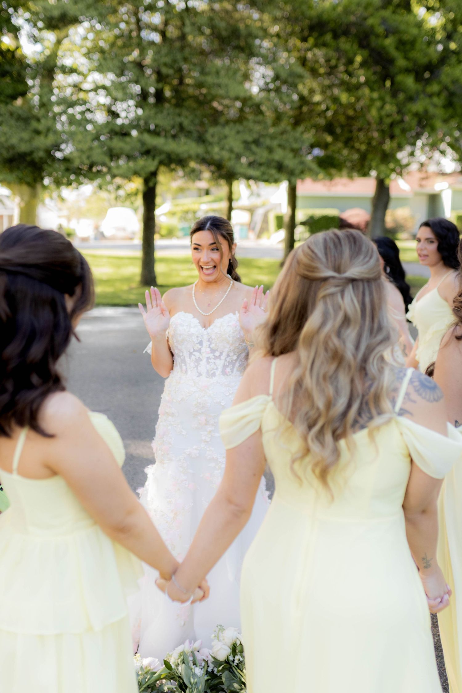 Bridesmaids in light colored dresses share a candid laughing moment together outdoors during a wedding photoshoot.