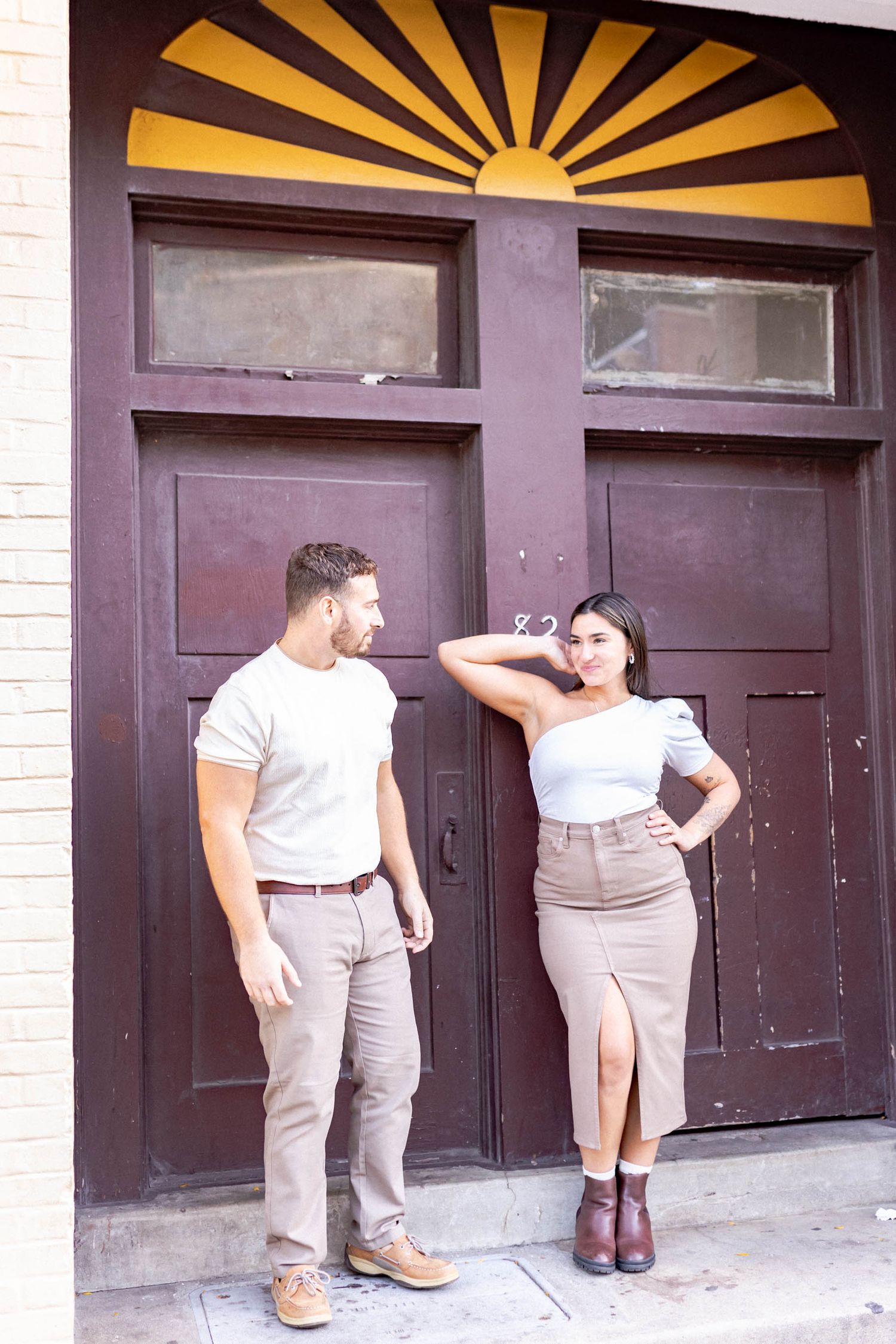 A couple poses playfully in front of art deco style doors with yellow sunburst patterns.