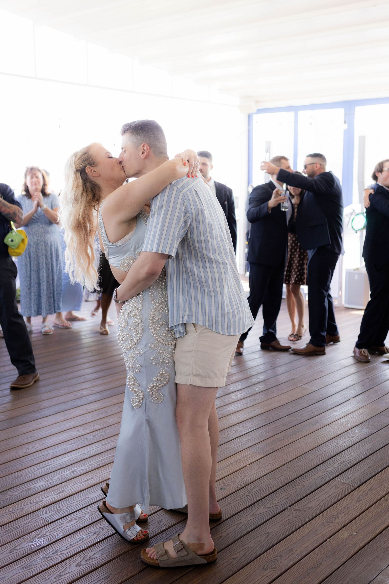 Sequence of couples dancing together on a wooden deck with large windows in the background.