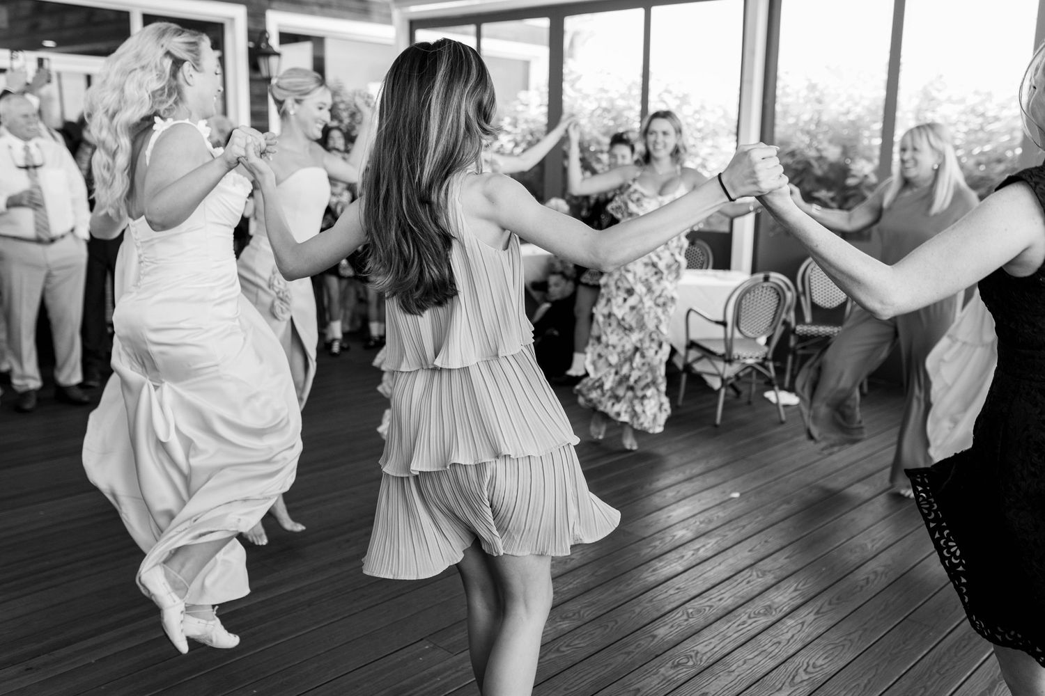 Wedding guests dancing together on a wooden dance floor at a reception celebration.