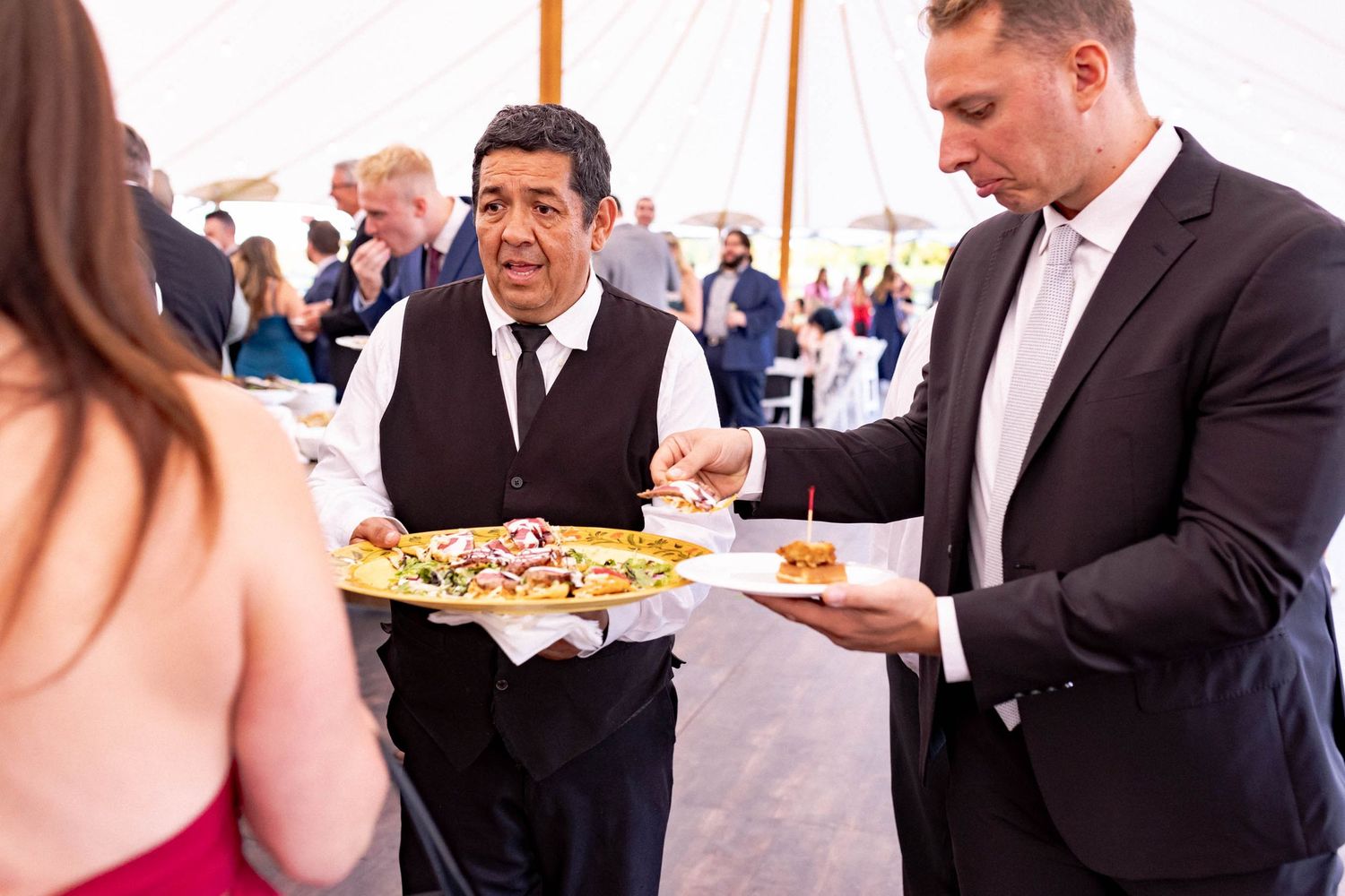 Guests in formal attire serve themselves food from platters at an elegant event reception.