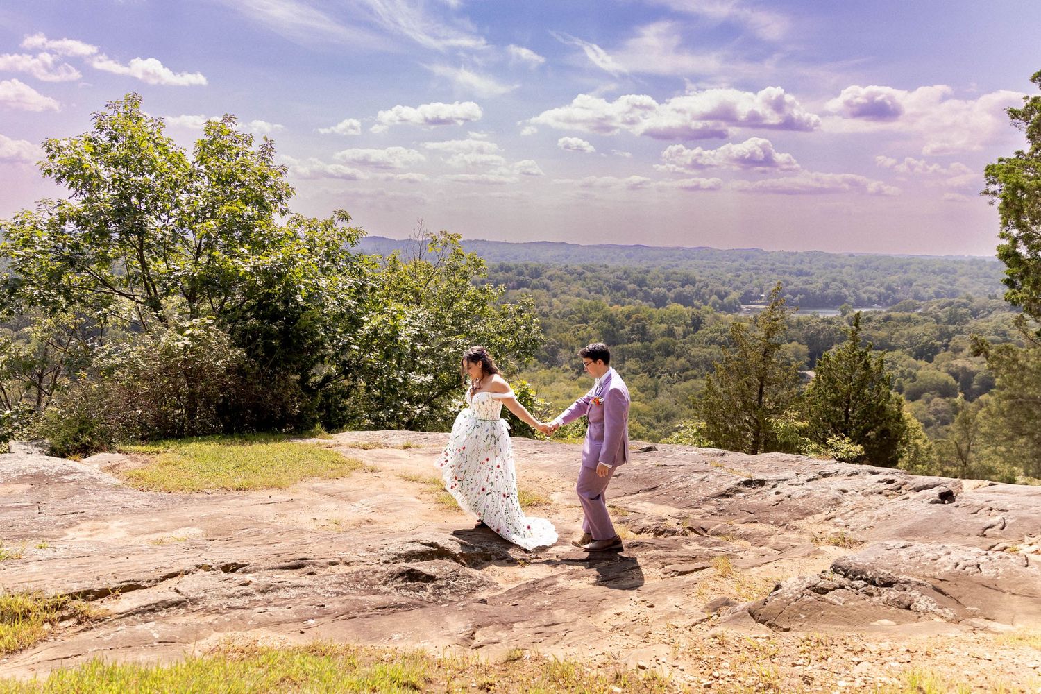 A romantic proposal takes place on a scenic mountain overlook with a sweeping valley view on a sunny afternoon.