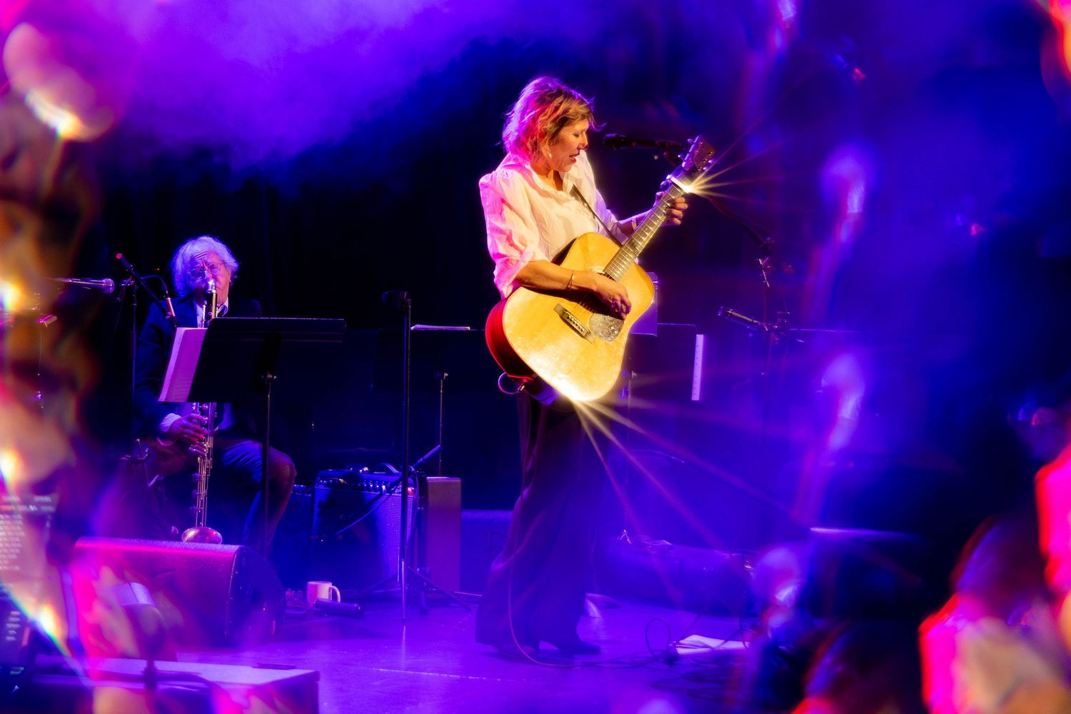 Concert performers on stage illuminated by vibrant purple lighting during a live music performance.
