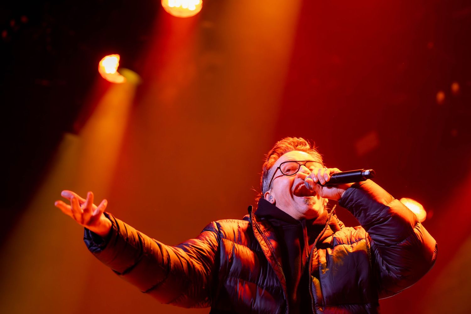 Concert performer silhouetted against dramatic red stage lighting during energetic live performance.