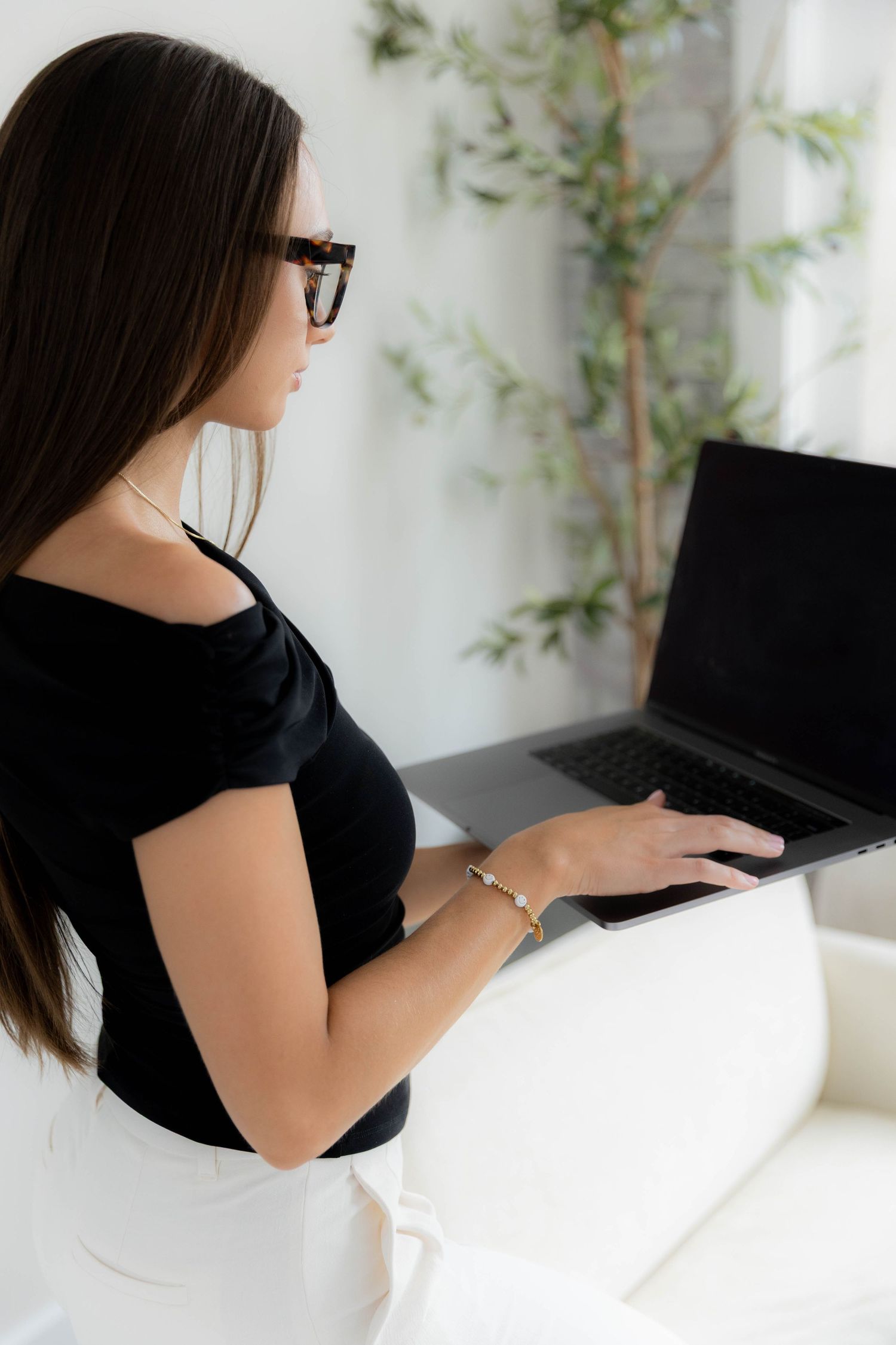 Person in black top working on laptop while seated on white furniture in minimalist setting.