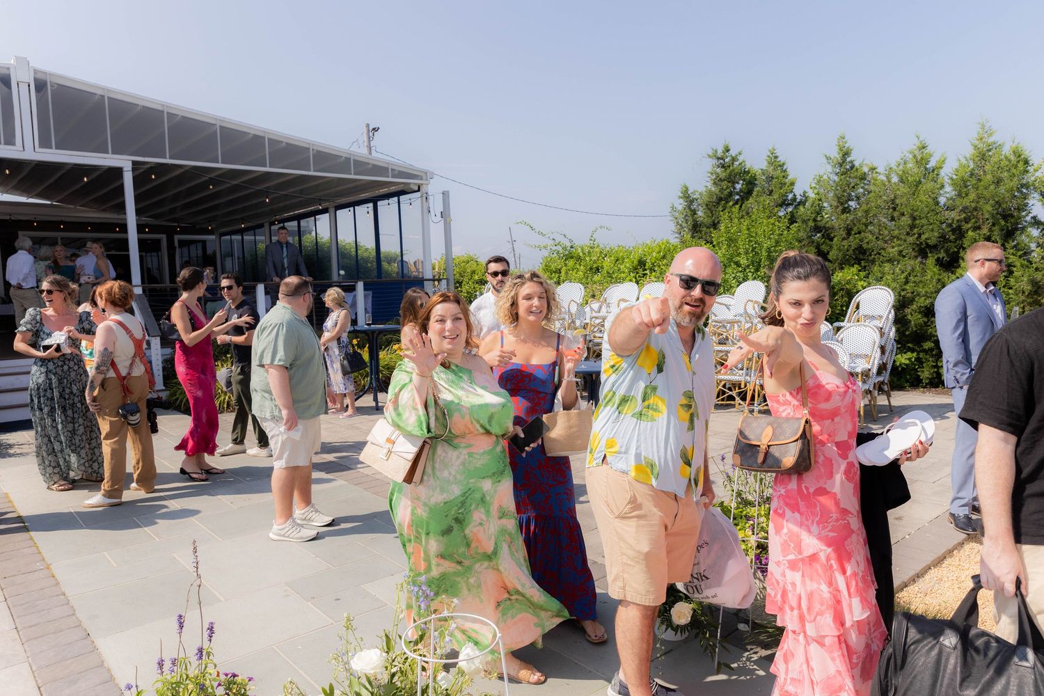 A group of people gather for a celebration at a modern waterfront venue with glass walls.