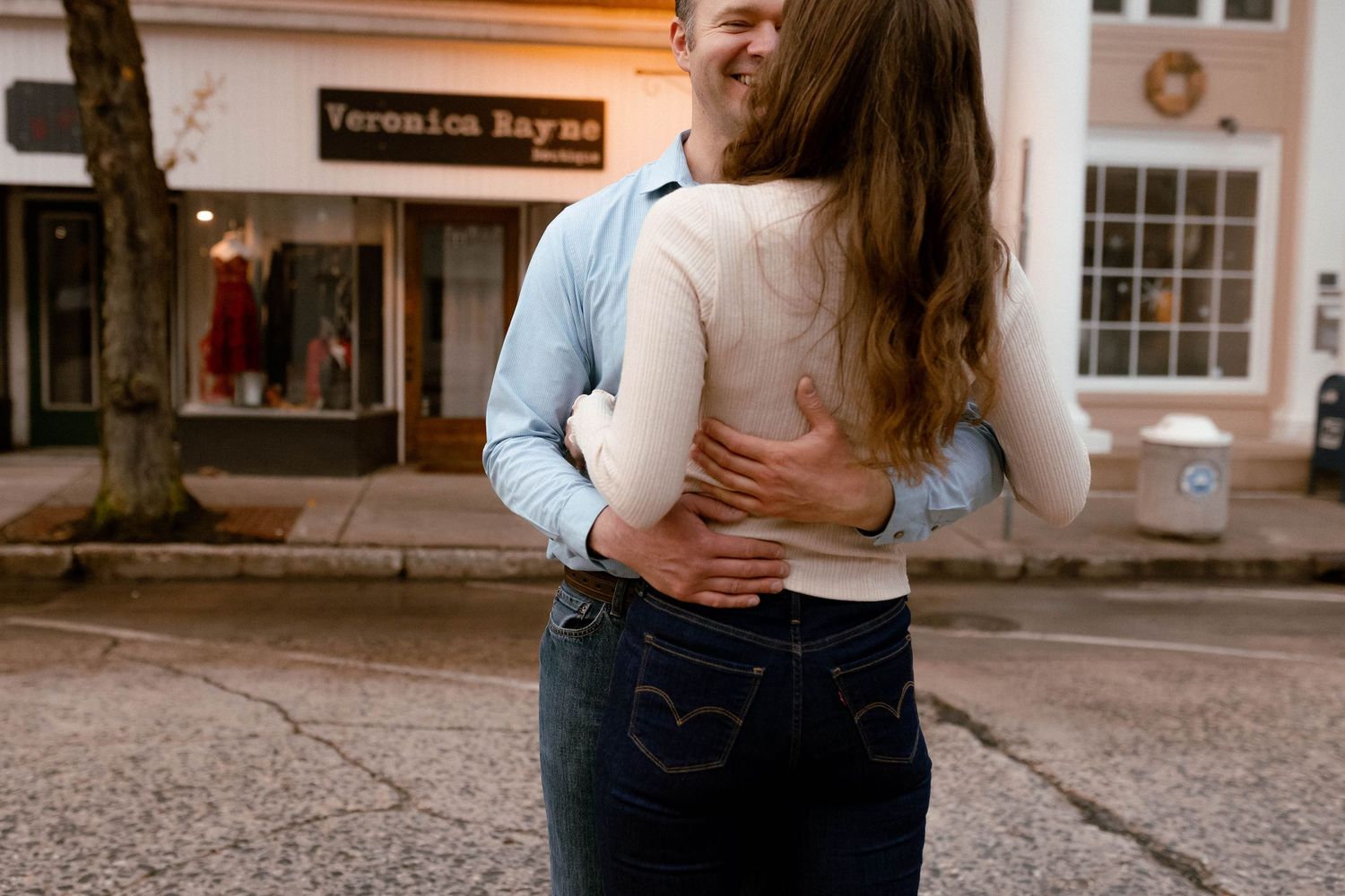 Two people embrace on a quaint downtown street during golden hour.