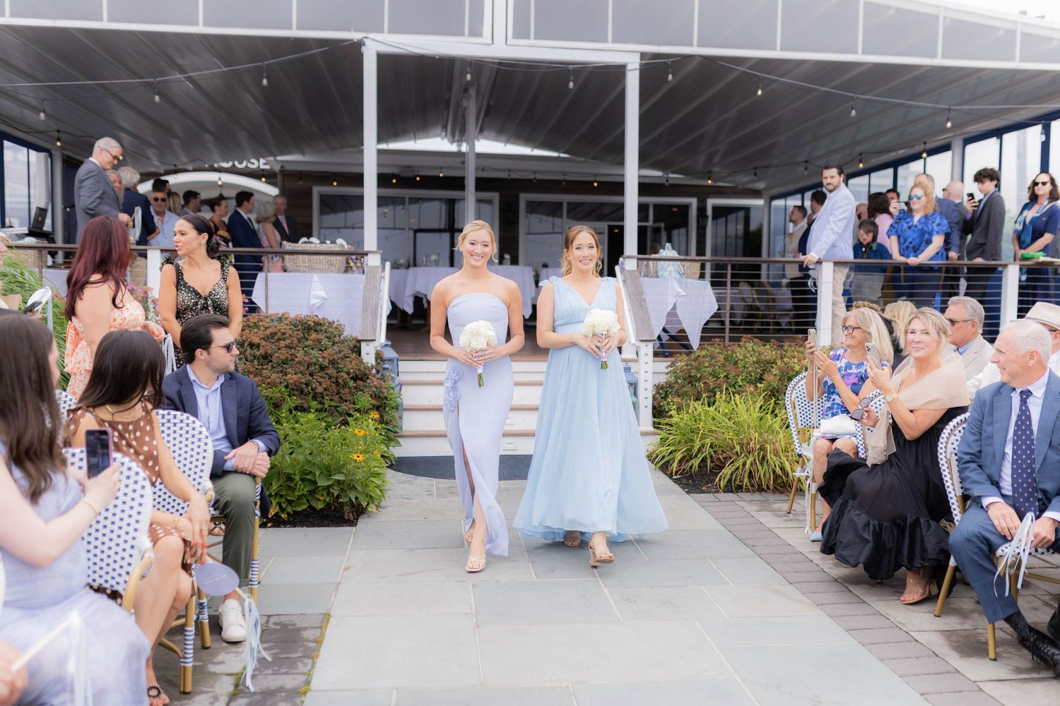 Wedding attendees watch as bridesmaids in light blue dresses walk down an outdoor aisle during a summer ceremony.