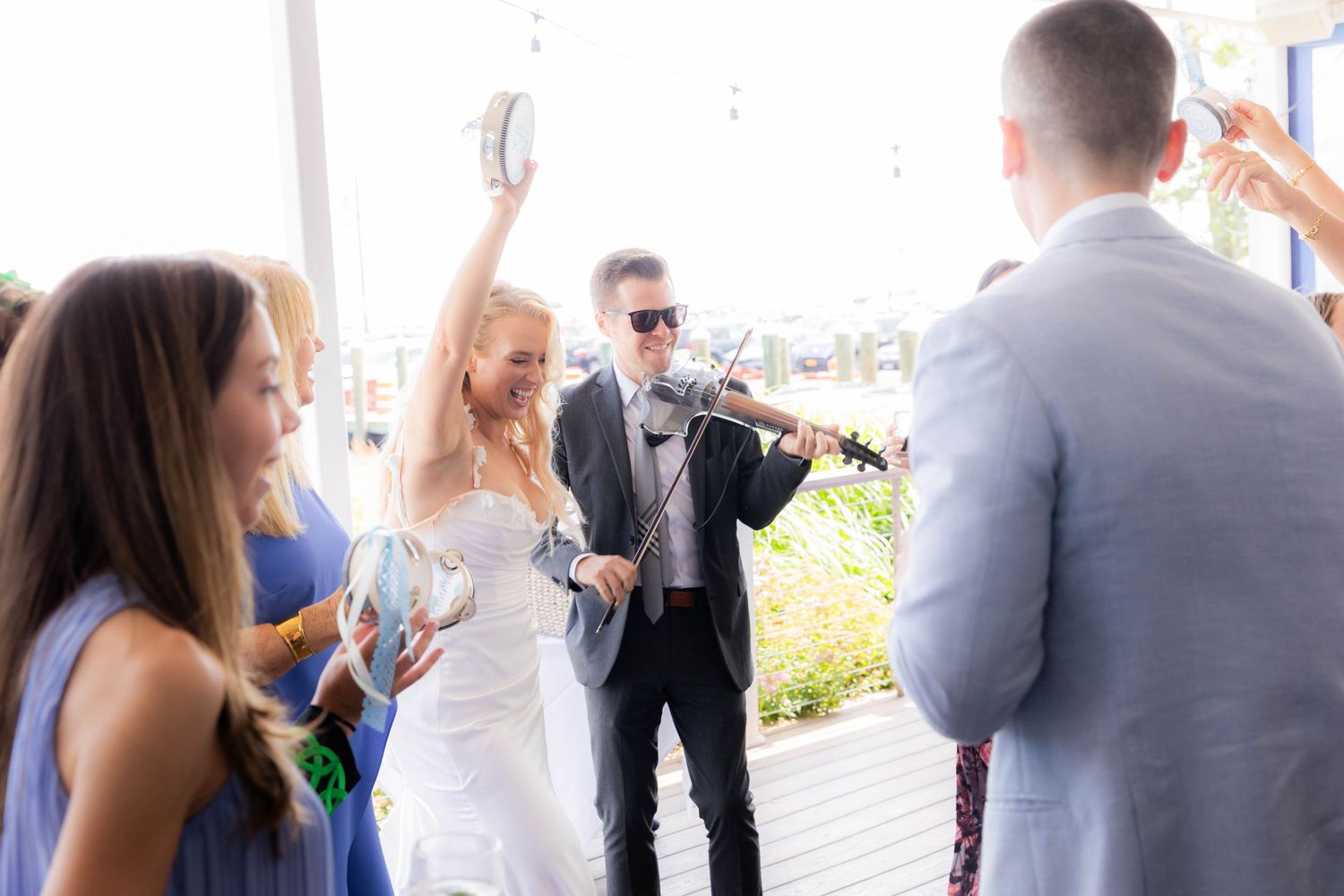 A group of wedding guests mingling and socializing on an outdoor patio during a sunny celebration.